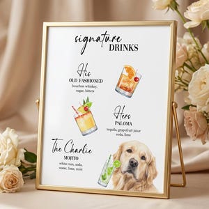 May include: A gold framed sign with the words "signature DRINKS" in elegant script. The sign features illustrations of cocktails and a golden retriever. The cocktails are labeled "His", "Hers", and "The Charlie".