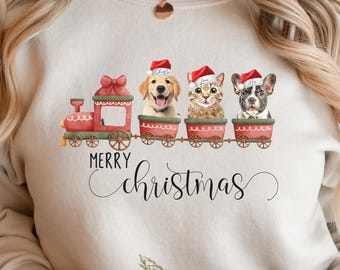 May include: Beige sweatshirt with a festive train design. The train cars feature a golden retriever, a cat, and a French bulldog, all wearing Santa hats. The words "Merry Christmas" are written below the train in a script font.