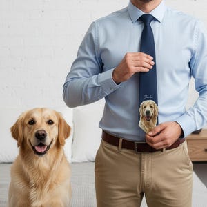 May include: A navy blue necktie featuring a custom portrait of a golden retriever dog and the name Charlie printed in white script. The tie is worn with a light blue button-down shirt and khaki trousers, paired with a golden retriever dog.