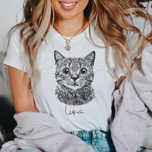 May include: A white t-shirt with a black and white illustration of a cat's face and the name "Luna" printed on the front.