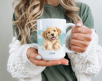 May include: A white ceramic mug featuring a watercolor-style illustration of a golden retriever puppy centered against a light blue abstract splash. The name Charlie is printed in a black script font below the puppy illustration on the mug.