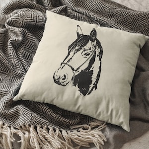 May include: A white pillow with a black and white illustration of a horse's head. The pillow is sitting on a black and white patterned blanket.
