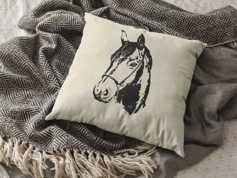 May include: A white pillow with a black and white illustration of a horse's head. The pillow is sitting on a black and white patterned blanket.