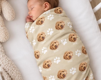 May include: A beige swaddle blanket featuring a repeating pattern of golden-brown dog faces and white paw prints. Each dog face is accompanied by the name Willow printed in white script. The fabric is wrapped around a sleeping infant.