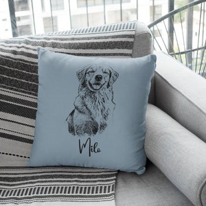 May include: A light blue throw pillow with a black and white illustration of a golden retriever dog. The dog is sitting and smiling. The pillow has the name "Milo" written in black cursive lettering.