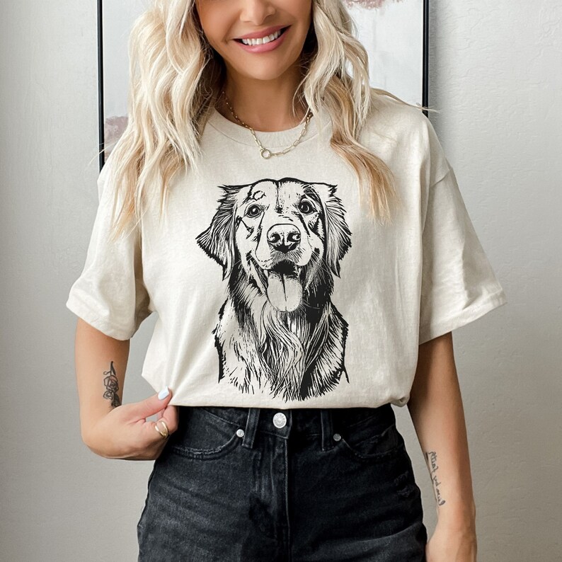 Beige t-shirt featuring a custom black-and-white sketch of a happy dog. Worn by a smiling woman paired with black jeans for a casual look. A perfect personalized gift for dog lovers or pet parents, combining style and a unique design.