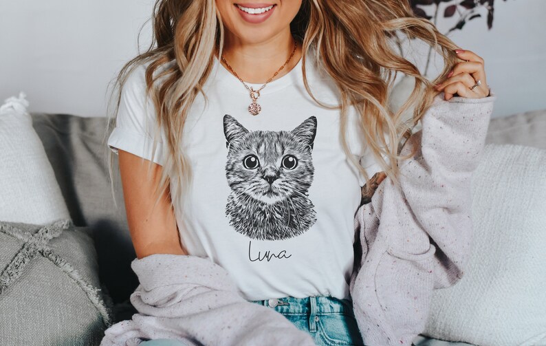 May include: White t-shirt with a black and white illustration of a cat's face and the name "Luna" printed below.