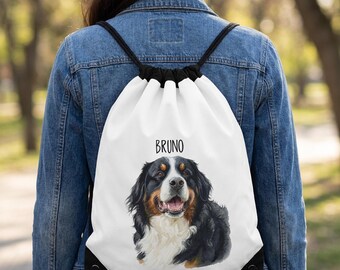 May include: A white drawstring backpack featuring a detailed illustration of a Bernese Mountain Dog with black, white, and brown fur. The name BRUNO is printed in black capital letters above the dog's head. The bag has black cord straps.