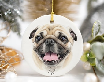 May include: A round white ceramic ornament featuring a detailed watercolor illustration of a tan pug with a black muzzle and an open mouth showing a pink tongue. The name Lucy is printed in black cursive script below the dog's chin.