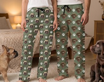 May include: Two pairs of lounge pants featuring an olive green background with a repeating pattern of brown pug faces and white paw prints. The pants have a black drawstring at the waist and are worn with plain white t-shirts.