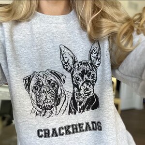 K&ouml;nnte beinhalten: Grauer Pullover mit einer Schwarzwei&szlig;illustration von zwei Hunden. Die Hunde sind ein Mops und ein Chihuahua. Der Text "CRACKHEADS" ist in schwarzen Buchstaben unter den Hunden gedruckt.