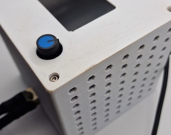 May include: White 3D printed box with a black knob and a blue dial. The box has a rectangular opening on the top and a grid of holes on the front.