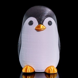 May include: A white and black penguin figurine with orange feet. The penguin is standing on a black surface.