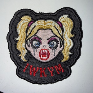 May include: An embroidered patch featuring a cartoon character with blonde pigtails, blue eyes, and dark makeup. The character has an open mouth showing fangs and red lips. Below the face, the red text reads IWKYM on a black background.