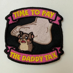 May include: An embroidered patch with a black background featuring a cartoon hamster with a shocked expression beneath a large foot. Pink banners at the top and bottom contain the yellow embroidered text TIME TO PAY and THE DADDY TAX.