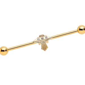 May include: Gold-colored industrial barbell earring featuring a decorative UFO charm with three clear gems. The barbell has a straight bar with a ball on each end. The UFO charm has a detailed design.