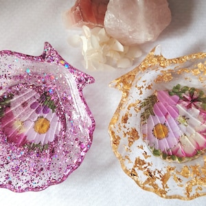 Può includere: Due portaoggetti a forma di conchiglia in resina con fiori pressati e glitter. Un portaoggetti è rosa con glitter iridescente e l'altro è dorato con foglia d'oro.