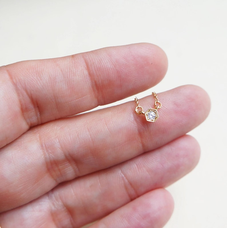 May include: A delicate gold chain necklace with a small, clear gemstone set in a hexagonal pendant.