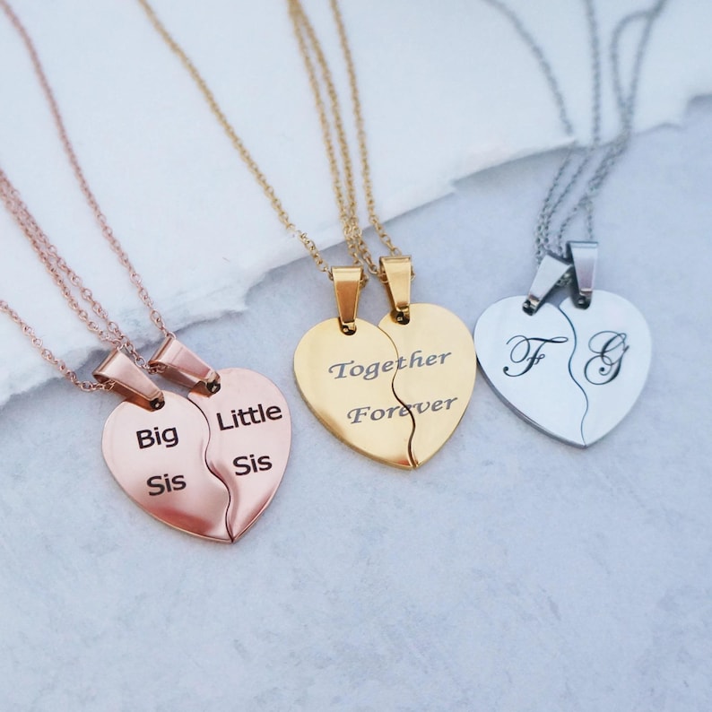 May include: Three sets of matching necklaces with heart-shaped pendants. One set features the words "Big Sis" and "Little Sis" on the pendants. Another set features the words "Together Forever" on the pendants. The third set features the letters "F" and "G" on the pendants.