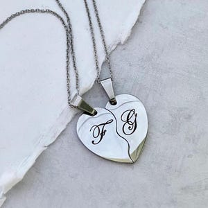 May include: Two silver necklaces with matching heart-shaped pendants. The pendants are split in half and engraved with the letters "F" and "G".