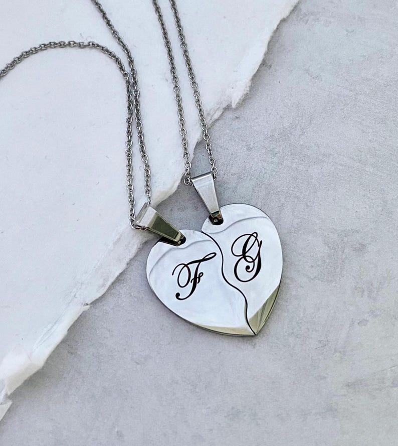 May include: Two silver necklaces with matching heart-shaped pendants. The pendants are split in half and engraved with the letters "F" and "G".