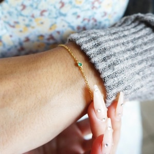 May include: A delicate gold chain bracelet with a small green gemstone.