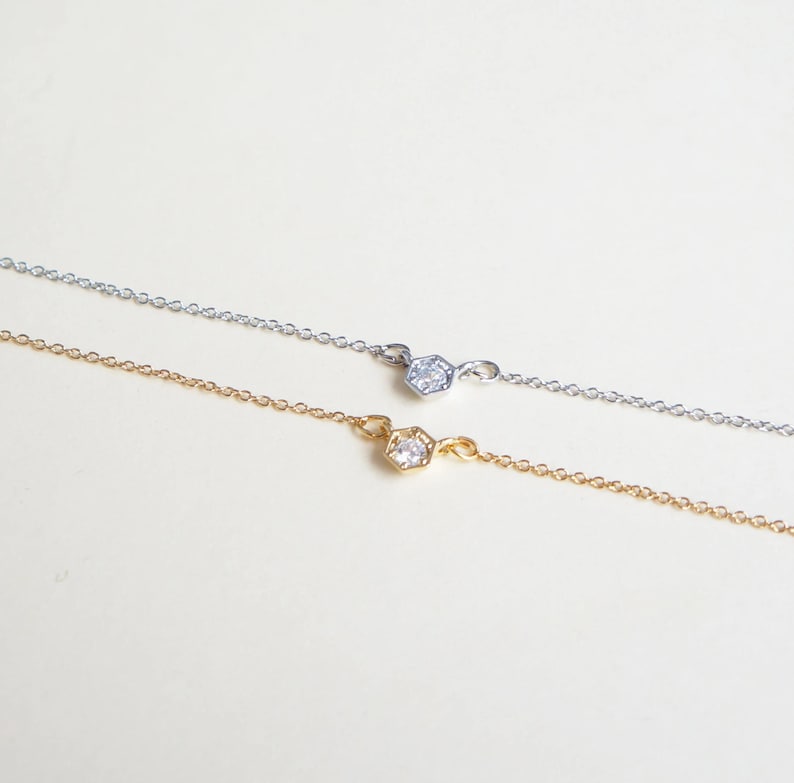 May include: Two delicate necklaces with a small, clear, hexagonal stone pendant. One necklace is silver and the other is gold.