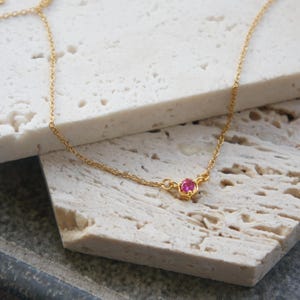 May include: A delicate gold chain necklace with a single pink gemstone pendant.