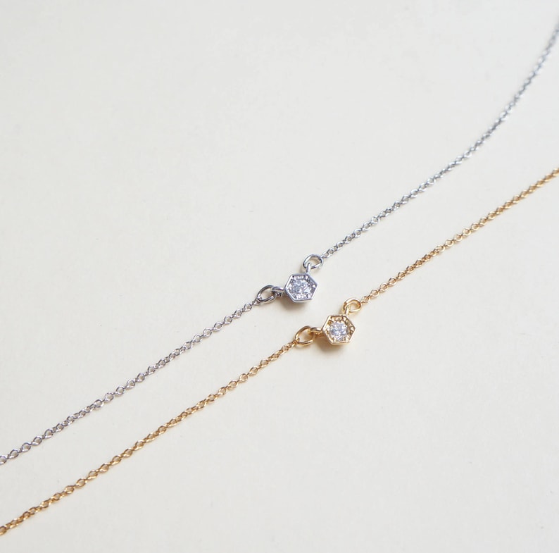 May include: Two delicate necklaces with a single diamond set in a hexagonal pendant. One necklace is silver and the other is gold.