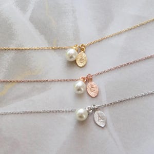 May include: Three delicate necklaces with pearl and leaf charms. The necklaces are in gold, rose gold, and silver.