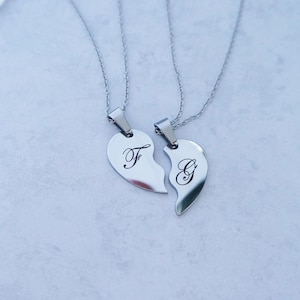 May include: Two silver necklaces with matching heart pendants. The pendants are broken hearts, one with the letter "F" and the other with the letter "G".