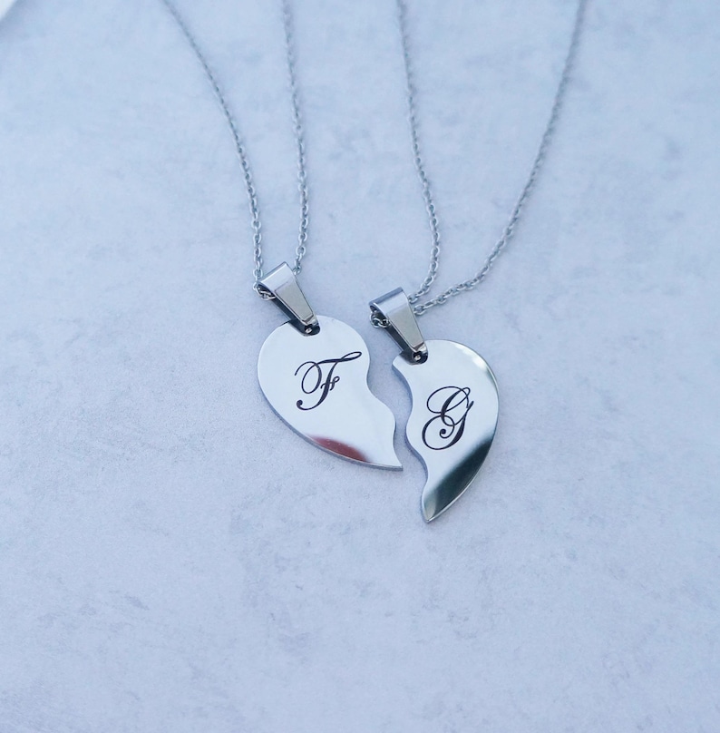 May include: Two silver necklaces with matching heart pendants. The pendants are broken hearts, one with the letter "F" and the other with the letter "G".