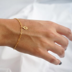May include: A gold chain bracelet with a gold letter 'G' charm.