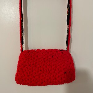 May include: A red crocheted handbag with a black and floral patterned strap.