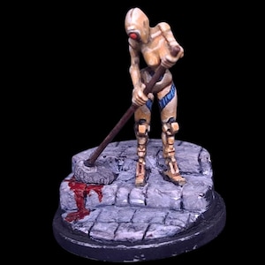 May include: A miniature figurine of a humanoid figure with a red eye, wearing gold and blue armour, holding a mop. The figure is standing on a stone base with a blood stain. The background is black.