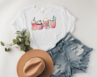 Op de afbeelding: Wit T-shirt met een afbeelding van vier verschillende roze en witte koffie drankjes, waarvan er één de tekst "Mum Fuel" heeft.