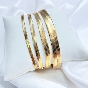 Puede incluir: Cuatro collares de cadena de serpiente de oro de diferentes anchos, mostrados sobre una superficie blanca.