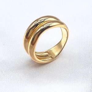 May include: A gold-colored ring with a double-band design. The ring has a smooth, polished surface and a rounded shape. The bands cross over each other, creating a unique and stylish look. The ring is likely made of a precious metal, such as gold.