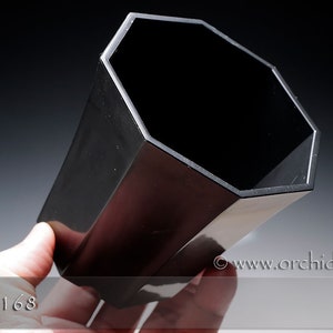 May include: A black octagonal plastic pot for growing orchids. The pot is empty and has a smooth, glossy finish.