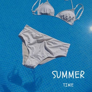 Puede incluir: Un conjunto de bikini blanco, compuesto por un top triangular y una braguita de cintura alta, flota sobre un fondo azul con azulejos. Las palabras "SUMMER TIME" están escritas en escritura blanca. La imagen evoca el verano y el ocio.
