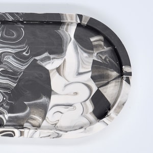May include: A black and white oval tray with a marbled design. The tray is made of resin and has a smooth, glossy finish.