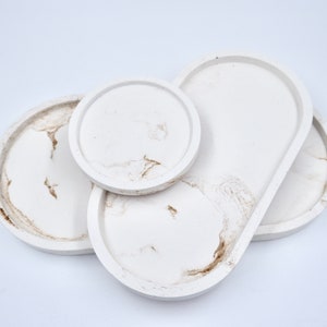 May include: Set of four white ceramic trays with a marbled design. The trays are in various shapes, including round and oval.