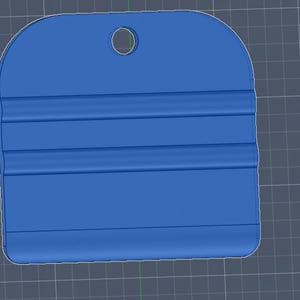 May include: A blue plastic squeegee tool featuring a rounded top edge with a centered circular hole for hanging. The body of the tool includes two horizontal raised ridges across the center, providing a grip surface for application tasks.