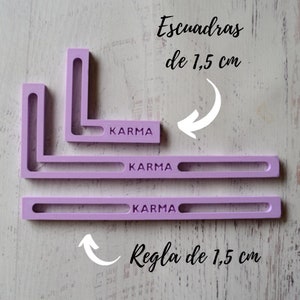 以下が含まれることがあります： ラベンダー色の直角定規3つとストレート定規。定規には「KARMA」の文字が印刷されています。画像内のテキストは「Escuadras de 1,5 cm」と「Regla de 1,5 cm」です。