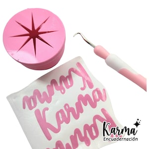 May include: Pink vinyl sticker with the word "Karma" written in a cursive font. The sticker is on a white sheet of paper. A pink tool with a hook on the end is also in the image. The tool is used to apply vinyl stickers. The image also includes a pink plastic circle with a star-shaped cutout.