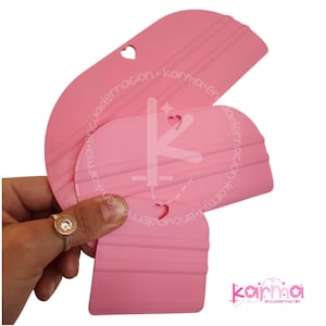 Op de afbeelding: Drie roze plastic gereedschappen met hartvormige uitsparingen. De gereedschappen hebben een gladde, afgeronde rand en zijn ontworpen om lijm of andere kleefstoffen te verspreiden.