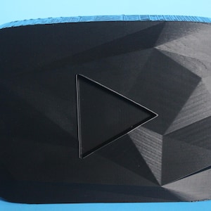 Op de afbeelding: Een zwart, 3D-geprint, geometrisch YouTube-logo met een play-knop uitsnijding. Het logo is gemaakt van een getextureerd, zwart plastic.