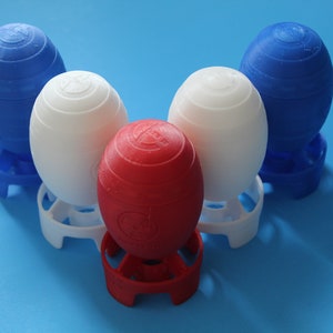May include: Four egg-shaped objects, each with a different color: blue, white, red, and blue. Each object is sitting on a stand that matches the color of the object. The objects are arranged in a triangular shape.