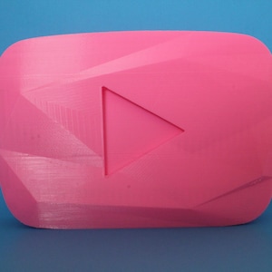 Pode incluir: Um logotipo do YouTube de plástico rosa impresso em 3D com um botão de reprodução no centro.