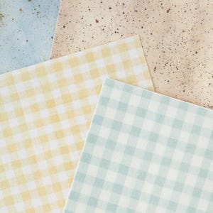 May include: An assortment of patterned paper sheets in various colors. The sheets include a light blue speckled design, a beige speckled design, a yellow gingham pattern, and a light blue gingham pattern.